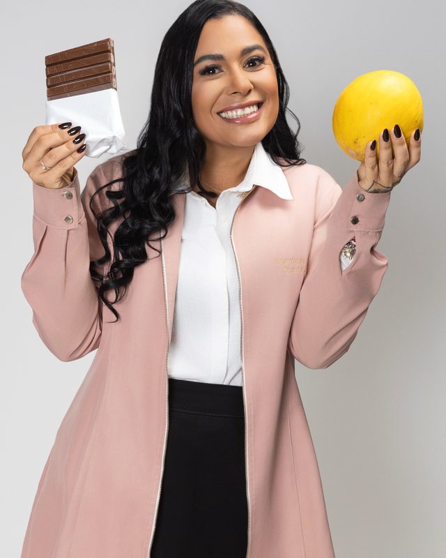 Monique Fahel segurando uma barra de chocolate numa mão e um melão na outra